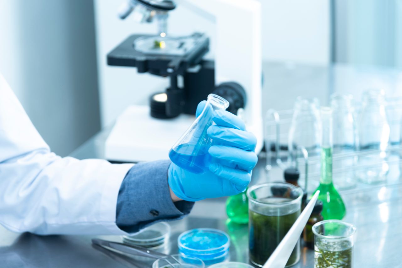 about-us Scientist in gloves analyzing blue liquid in a laboratory setting with microscope and glassware.