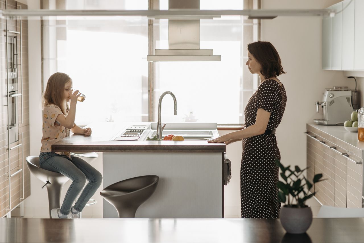 services-02 A mother and daughter share a moment in a bright, modern kitchen with juice and fresh fruit.